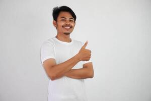 retrato de alegre asiático hombre en vistiendo blanco t camisa sonriente y demostración pulgares arriba a cámara aislado terminado blanco antecedentes foto