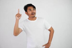emocionado joven asiático hombre señalando dedos arriba teniendo un bueno idea con Copiar espacio vistiendo blanco t camisa aislado en blanco antecedentes foto