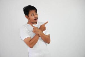 Shocked young Asian man crossed arms and points sideways, chooses between two options, indicates left and right wearing white t shirt isolated on white background photo