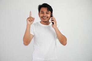 emocionado joven asiático hombre señalando dedos arriba teniendo un bueno idea con mientras vocación vistiendo blanco t camisa aislado en blanco antecedentes foto