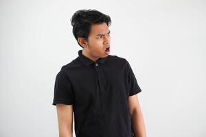 enojado asiático hombre abierto boca en lado vistiendo negro polo t camisa aislado en blanco antecedentes foto