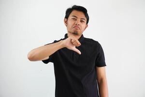 joven asiático hombre demostración pulgar abajo firmar con negativo expresión vistiendo negro polo t camisa aislado en blanco antecedentes foto