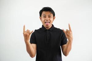 smiling Young handsome asian man wearing black polo t shirt and shouting with crazy expression doing gesture rock symbol with hands up. Music star. Heavy concept. isolated on white background photo