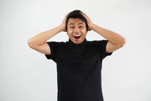 young asian man both hands holding the head screaming, very excited, passionate, satisfied with something, wearing black polo t shirt isolated on white background photo