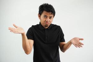 Portrait of handsome young asian man confused puzzled man shrugging shoulders wearing black polo t shirt isolated over white background photo