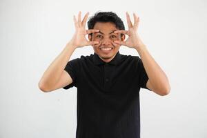 joven asiático hombre posando acuerdo ojos abrió a encontrar un éxito oportunidad, vistiendo negro polo t camisa aislado en blanco antecedentes foto