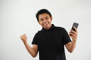 Excited happy young asian man winner feeling joy using smartphone winning lottery game, betting, getting cash back online gift in mobile app message holding cell phone isolated on white background. photo