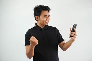 Excited happy young asian man winner feeling joy using smartphone winning lottery game, betting, getting cash back online gift in mobile app message holding cell phone isolated on white background. photo