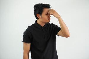 Casual young asian man against a vibrant white studio background, having a head ache, touching front of the face, wearing black polo t shirt photo