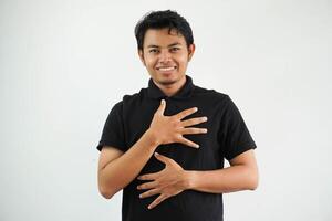 sonriente joven asiático hombre se ríe felizmente y tiene divertido acuerdo manos en cofre y estómago vistiendo negro polo t camisa aislado en blanco antecedentes foto