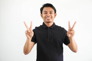 joven asiático hombre sonriente contento con ambos mano demostración paz firmar vistiendo negro polo t camisa aislado en blanco antecedentes foto