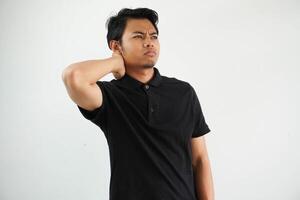 young asian man in black polo t shirt, white studio backdrop having a neck pain due to stress, massaging and touching it with hand. photo