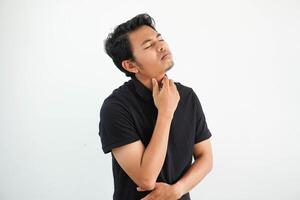 young asian man posing on a white backdrop wearing black polo t shirt suffers pain in throat due a virus or infection. health care concept photo