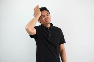 Portrait of young asian man isolated on white background suffering from severe headache, pressing fingers to temples, closing eyes to relieve pain with helpless face expression photo