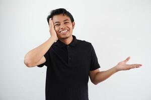 young asian man holds copy space on a palm, keep hand over cheek. Amazed and delighted, wearing black polo t shirt isolated on white background photo