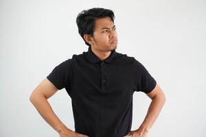 young Asian man showing disappointed expression with both hand on his waist wearing black polo t shirt isolated on white background photo