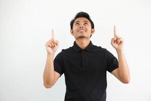 joven asiático hombre sonriente contento y señalando ambos manos arriba vistiendo negro polo t camisa aislado en blanco antecedentes foto