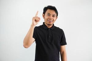 sonriente joven asiático hombre señalando arriba con contento cara expresión vistiendo negro polo t camisa aislado en blanco antecedentes foto