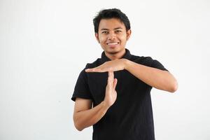 young asian man in black polo t shirt, studio shot on white backdrop showing a timeout gesture. photo