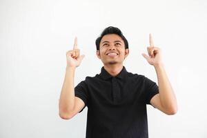 joven asiático hombre sonriente contento y señalando ambos manos arriba vistiendo negro polo t camisa aislado en blanco antecedentes foto