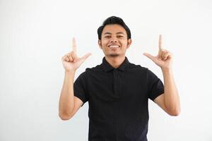 joven asiático hombre sonriente contento y señalando ambos manos arriba vistiendo negro polo t camisa aislado en blanco antecedentes foto