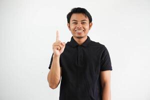 smiling young asian man pointing up with happy face expression wearing black polo t shirt isolated on white background photo