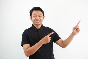 young asian man smiling confident with both hand pointing to the left side wearing black polo t shirt isolated white background photo