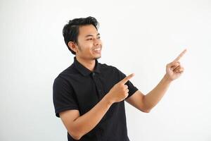 young asian man smiling confident with both hand pointing to the left side wearing black polo t shirt isolated white background photo