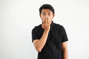 joven asiático hombre cerca su boca con manos y demostración conmocionado expresión vistiendo negro polo t camisa aislado en blanco antecedentes foto
