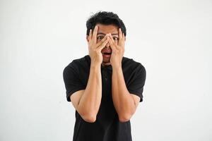 joven asiático hombre aislado en blanco antecedentes parpadeo mediante dedos asustado y nervioso, vistiendo negro polo t camisa. foto