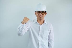 smiling or happy young asian man with clenched fist in white shirt and helmet,concept of male civil construction worker, builder, architect, mechanic, electrician posing for successful career. photo