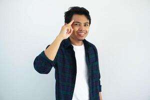 young asian man smiling at the camera while pointing to his temple isolated on white background. photo