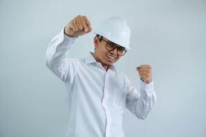 sonriente o contento joven asiático hombre con apretado puño en blanco camisa y casco,concepto de masculino civil construcción obrero, constructor, arquitecto, mecánico, electricista posando para exitoso carrera profesional. foto