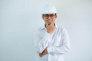 joven asiático masculino ingeniero vistiendo blanco difícil sombrero participación barbilla pensando para construcción trabajo aislado en blanco fondo, Copiar espacio. foto