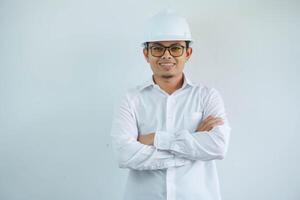 joven asiático hombre es ingeniero vistiendo casco en pie con cruzado brazos y sonriente con seguro, arquitecto o contratista, trabajador o mano de obra, industrial concepto. foto