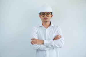 joven asiático hombre es ingeniero vistiendo casco en pie con cruzado brazos y sonriente con seguro, arquitecto o contratista, trabajador o mano de obra, industrial concepto. foto