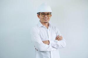 joven asiático hombre es ingeniero vistiendo casco en pie con cruzado brazos y sonriente con seguro, arquitecto o contratista, trabajador o mano de obra, industrial concepto. foto