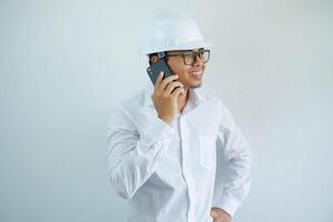 smiling or happy young asian man architect wearing white helmet hard hat when calling with someone isolated on white background. photo