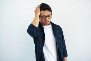 Asian youth with glasses showing pained expression while touching his head isolated on white background. photo