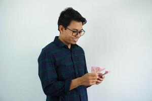 young asian man smiling happy when counting money that he hold isolated on white background photo