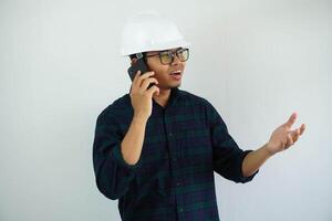 young Asian male engineer wearing white hard hat was talking on a cell phone for construction work isolated on white background, copy space. photo