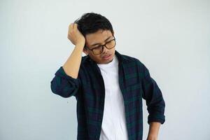 Asian youth with glasses showing pained expression while touching his head isolated on white background. photo