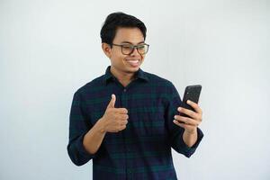 joven asiático hombre sonriente y dar pulgar arriba mientras participación móvil teléfono aislado en blanco antecedentes. foto