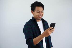 sonriente o contento cara joven asiático hombre mientras utilizando móvil teléfono aislado blanco antecedentes foto