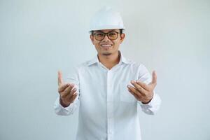 architect young asian man wearing white helmet standing over isolated white background smiling friendly open arms welcoming. Successful business. photo