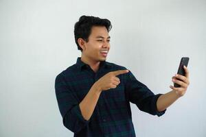 smiling young asian man showing happy face expression while pointing to mobile phone that he hold isolated on white background photo