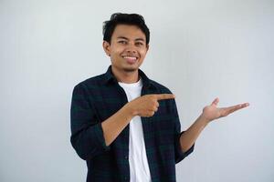 smiling young asian man while pointing to his open hand palm isolated on white background photo