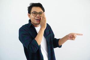 young asian man whispering something with happy expression and pointing to the left side isolated on white background photo