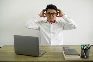 young asian businessman in a workplace frustrated and takes hands on head wearing white shirt with glasses isolated photo