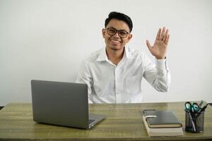 young asian businessman in a workplace saluting with hand with happy expression wear white shirt with glasses isolated photo
